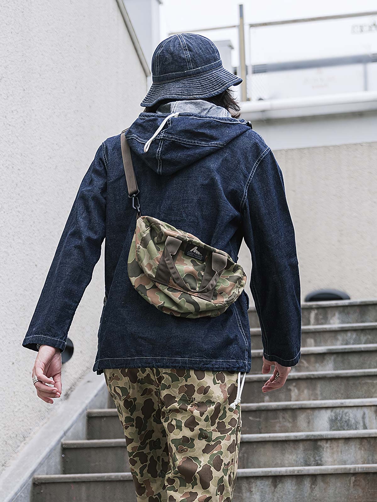 詳細画像: 大きなフードと三層前立てデザインのディテール特写。機能性とヴィンテージ感が際立つディテール。
モデル画像: モデルが迷彩柄砲兵防護プルオーバーパーカーを着用したスタイリング例。戦時風デザインを取り入れたコーディネート。