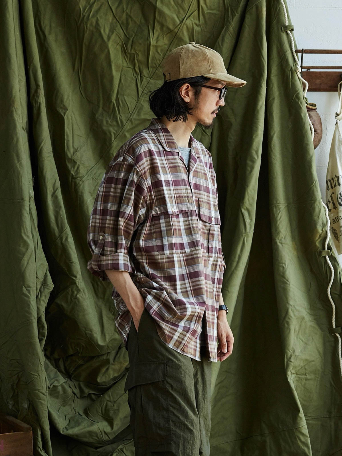 詳細画像: キューバンカラーと胸前のフラップポケットのディテール。チェック柄の鮮明さとシャツの質感を強調。
モデル画像: モデルがMADRAS (マドラス) チェック柄シャツを着用したスタイリング例。実際の着用感やフィット感を視覚的に伝える。