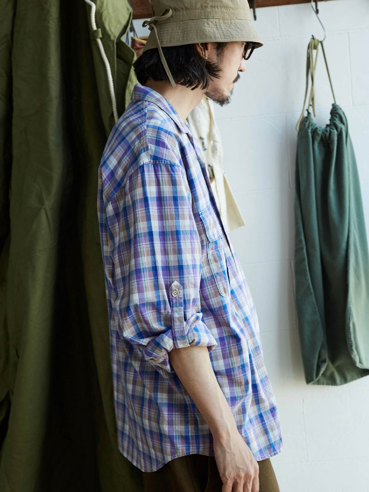 詳細画像: キューバンカラーと胸前のフラップポケットのディテール。チェック柄の鮮明さとシャツの質感を強調。
モデル画像: モデルがMADRAS (マドラス) チェック柄シャツを着用したスタイリング例。実際の着用感やフィット感を視覚的に伝える。