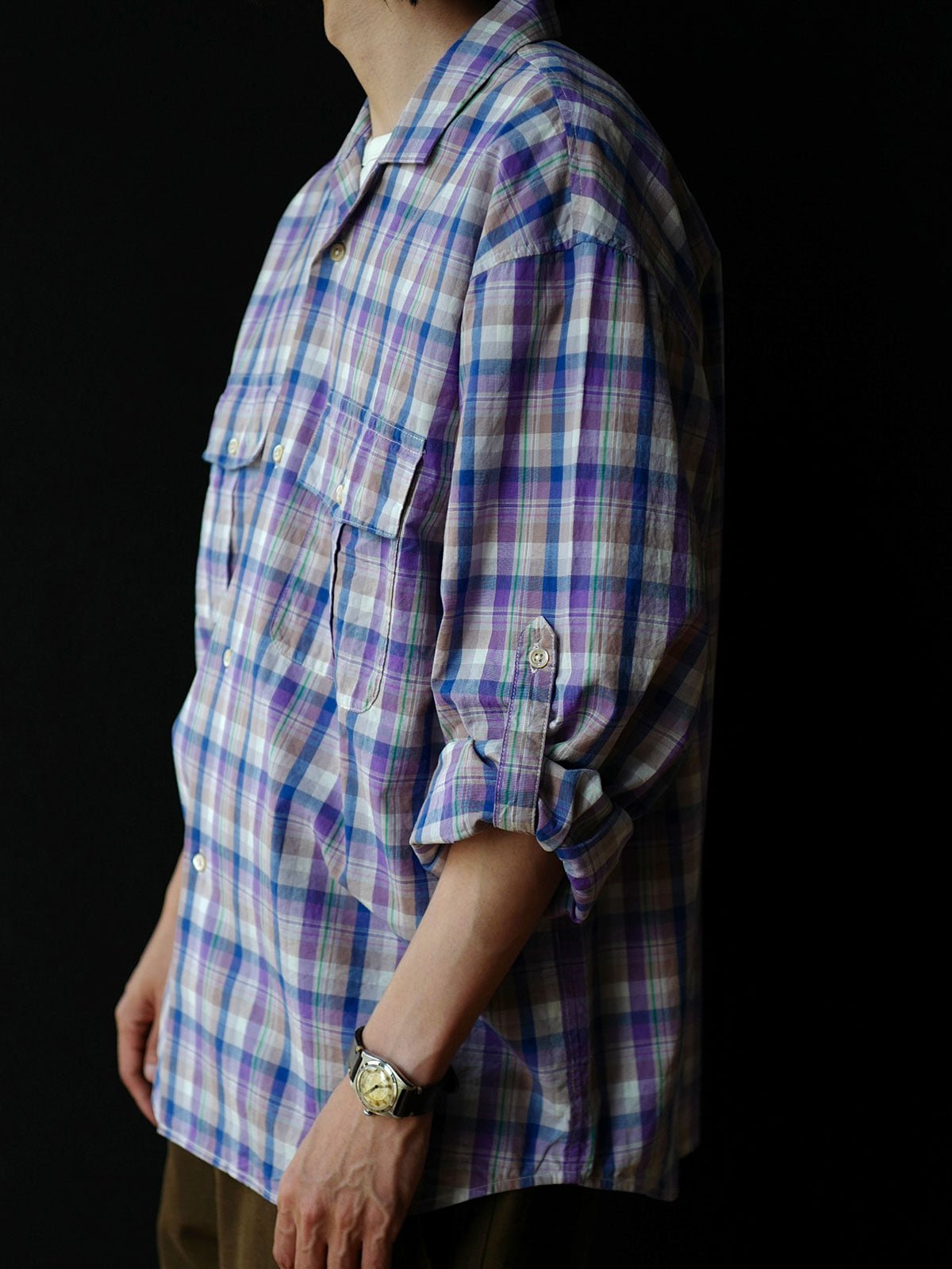 詳細画像: キューバンカラーと胸前のフラップポケットのディテール。チェック柄の鮮明さとシャツの質感を強調。
モデル画像: モデルがMADRAS (マドラス) チェック柄シャツを着用したスタイリング例。実際の着用感やフィット感を視覚的に伝える。