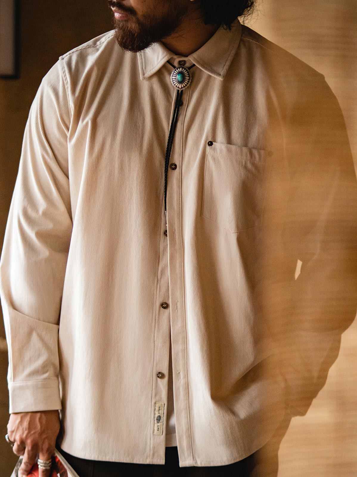 詳細画像:胸元のリベットデザインと裾のNAVAJOラベル。ヴィンテージ感のあるディテール。
モデル画像:モデルが着用したコーデュロイシャツの全身コーディネート。秋冬向けのカジュアルなルーズフィットスタイル。