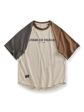 パッチワークとラグランスリーブ、カーブヘムが特徴の「SONG OF PEACE」プリント入りコットンTシャツ