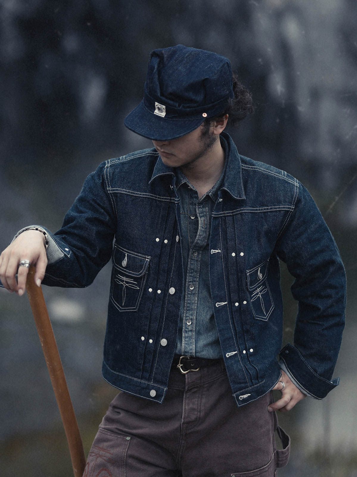 詳細画像: ボックスプリーツとラウンドリベットのディテールクローズアップ
モデル画像: インディゴデニムジャケットを着用したスタイリング例