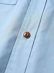 製品画像: クラシックなスタンドカラーと肘パッチが特徴のワークシャツ。シンプルでありながらスタイリッシュなデザインが際立っています。
詳細画像: 非対称ポケットと肘パッチが施されたディテール。デザインと機能性が融合した袖部分が強調されています。