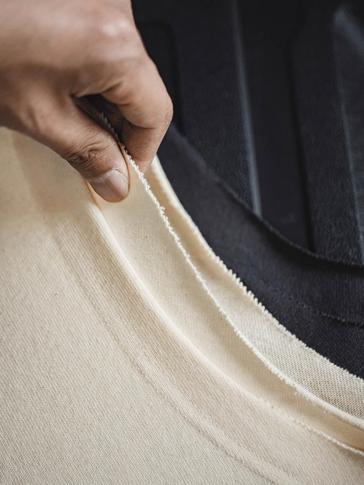 ヘビーウェイトのコットンハスク素材の詳細とダブルレイヤーのアームホールのクローズアップ。素材の厚みと耐摩耗性を強調し、デザインの階層感を示しています。