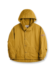 タスロン素材のシワ加工が特徴的な薄手フード付きジャケット全体画像。エポレットデザインとヴィンテージ感漂うテクスチャーが、アウトドアや日常のあらゆるシーンで活躍する一着。
詳細画像
スタンドカラーと折り襟の2WAY仕様、エポレットディテール、フラップ付きスナップボタンポケット、そしてドローコード付き裾のディテールを強調したクローズアップ画像。機能性とデザイン性が融合した細部。