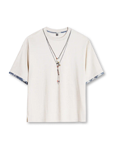 オフホワイトのTシャツ、胸元に重ねたネックレス柄のプリントと袖口の襤褸柄