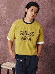 モデルがフットボールカルチャープリントTシャツを着用し、ジンジャーイエローのバリエーションで、ダークカラーのカジュアルパンツとスポーツシューズを合わせたカジュアルなスタイリングでポーズをとる画像。レトロかつ現代的な夏の装いを演出。