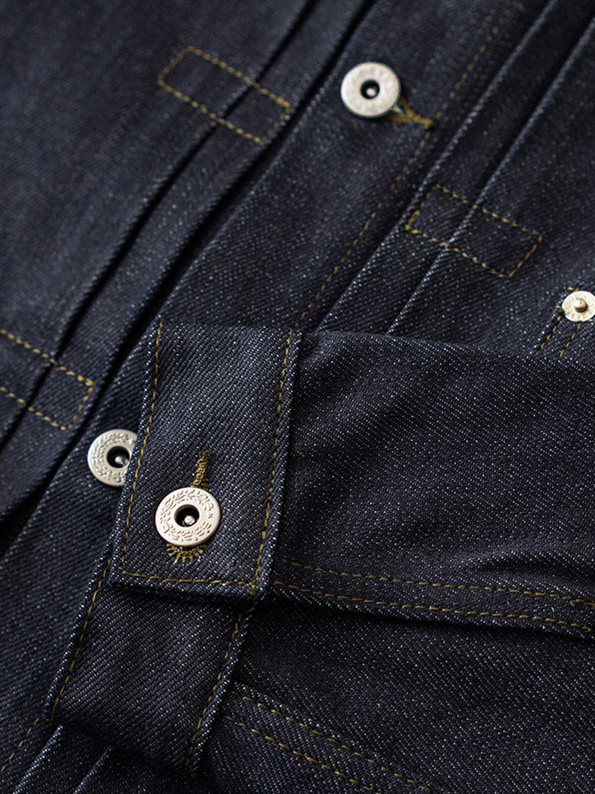 ジャケットのディテールショット、真鍮の未加工の錫メッキパリボタンとスラブデニムの質感を展示