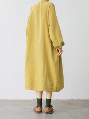 モデルがマスタードイエローのVネックリネンコットンドレスを着用し、自然で優雅なスタイルを披露