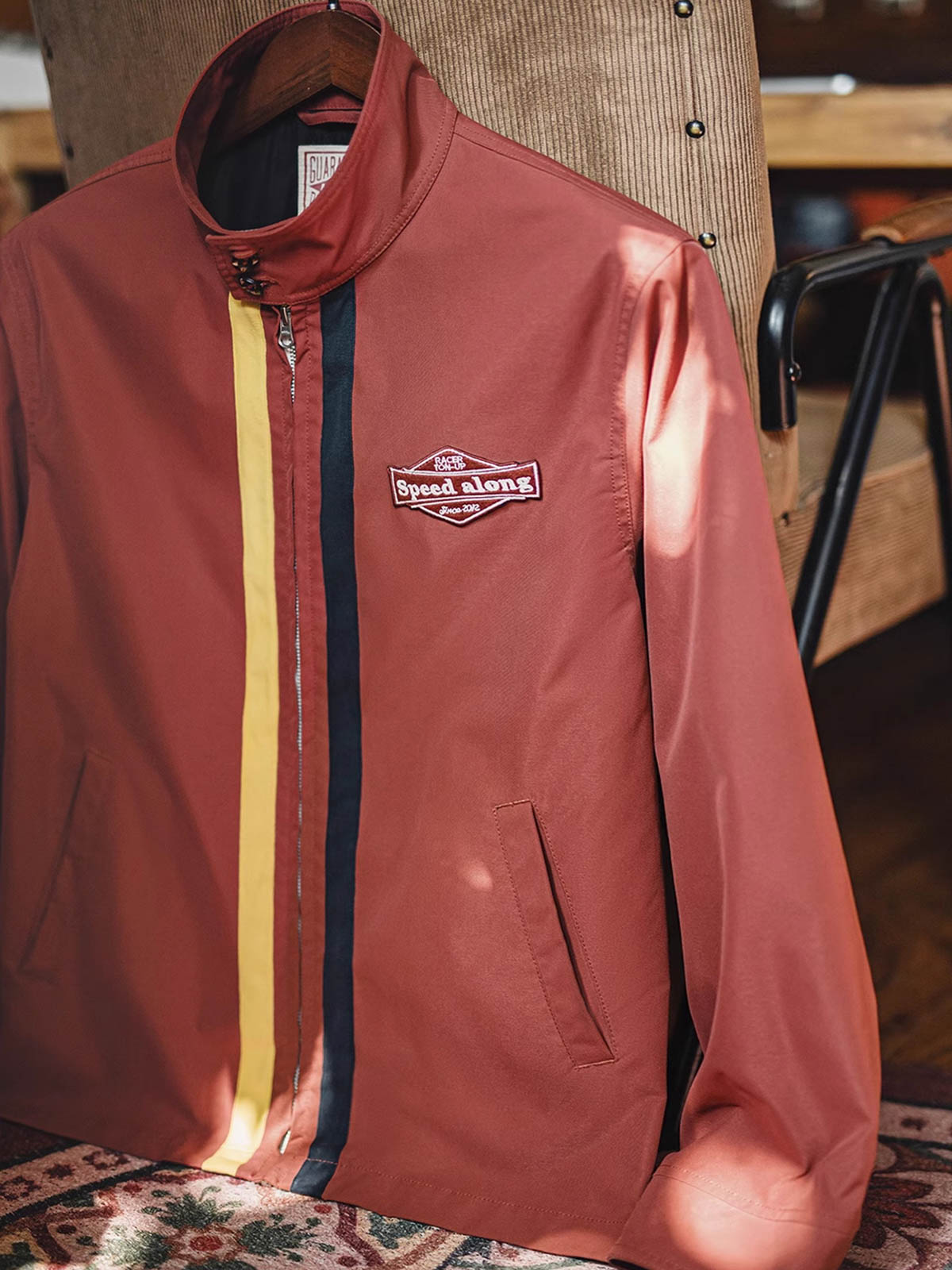 製品画像: 60年代風レトロデザインのバイカラーレーシングジャケット、スポーティーなスタンドカラーと耐久性あるツイル素材。
詳細画像: バイカラーのジッパーディテール、ツイル素材の高い耐摩耗性とレトロな赤色の特徴が分かる部分アップ。