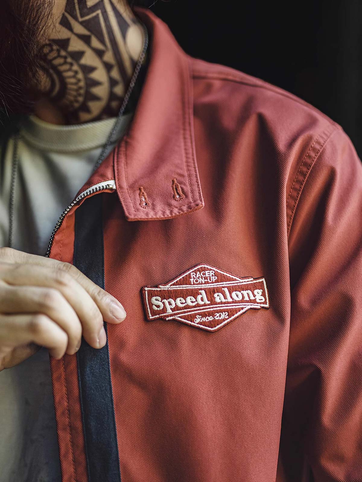 製品画像: 60年代風レトロデザインのバイカラーレーシングジャケット、スポーティーなスタンドカラーと耐久性あるツイル素材。
詳細画像: バイカラーのジッパーディテール、ツイル素材の高い耐摩耗性とレトロな赤色の特徴が分かる部分アップ。