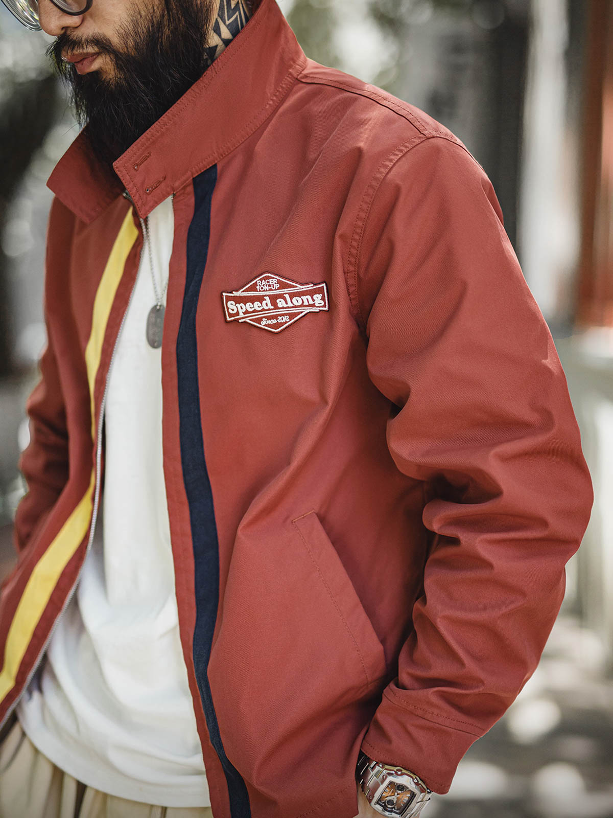 詳細画像: バイカラーのジッパーディテール、ツイル素材の高い耐摩耗性とレトロな赤色の特徴が分かる部分アップ。
モデル画像: レトロなレーシングジャケットを着用したモデル、ストリートファッションとヴィンテージスタイルを演出。