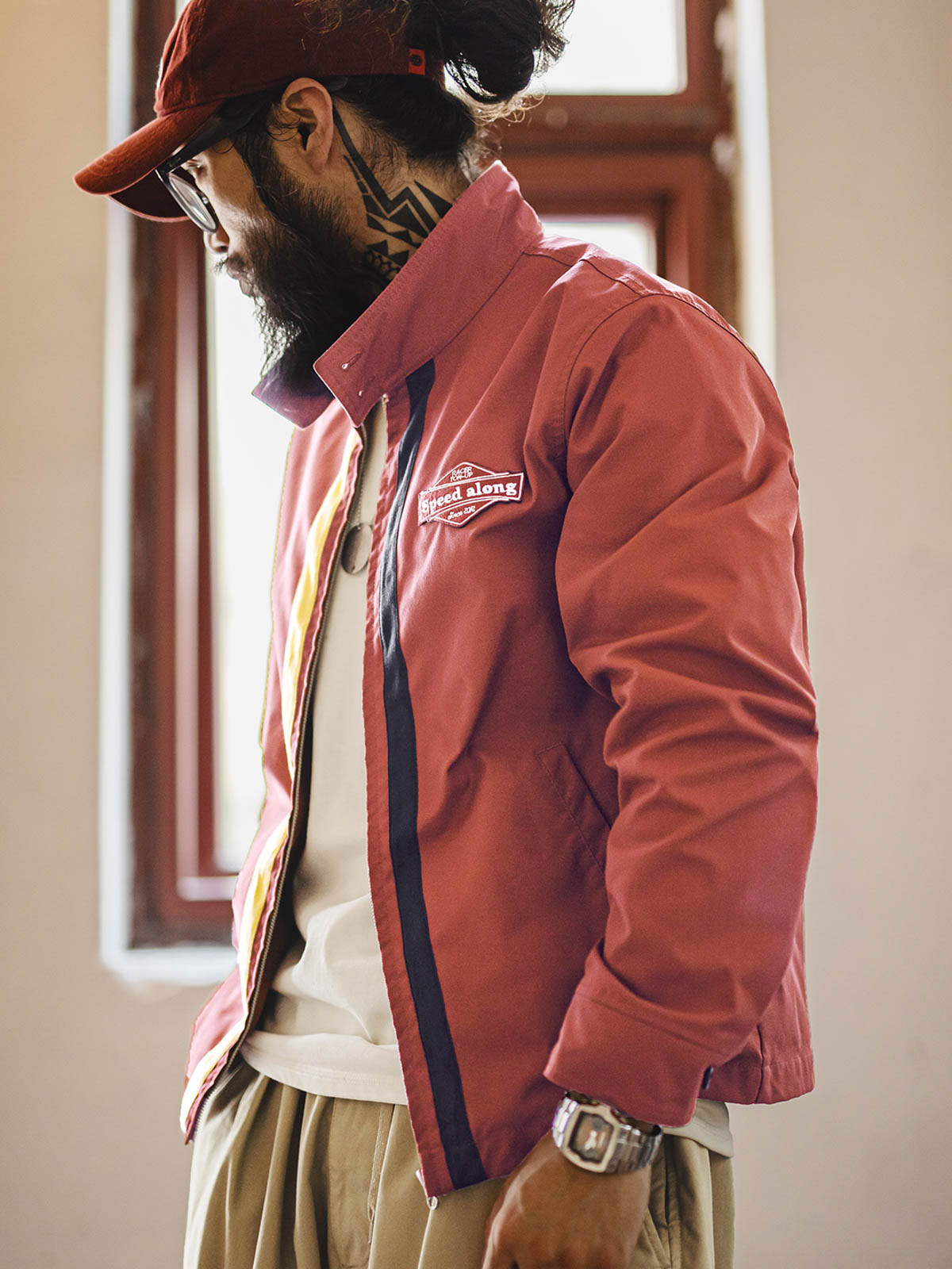 詳細画像: バイカラーのジッパーディテール、ツイル素材の高い耐摩耗性とレトロな赤色の特徴が分かる部分アップ。
モデル画像: レトロなレーシングジャケットを着用したモデル、ストリートファッションとヴィンテージスタイルを演出。