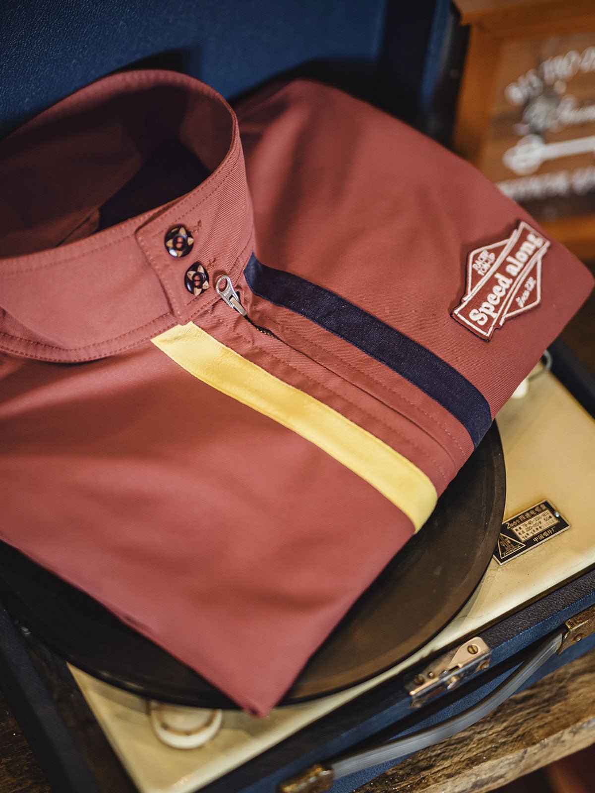 製品画像: 60年代風レトロデザインのバイカラーレーシングジャケット、スポーティーなスタンドカラーと耐久性あるツイル素材。
詳細画像: バイカラーのジッパーディテール、ツイル素材の高い耐摩耗性とレトロな赤色の特徴が分かる部分アップ。