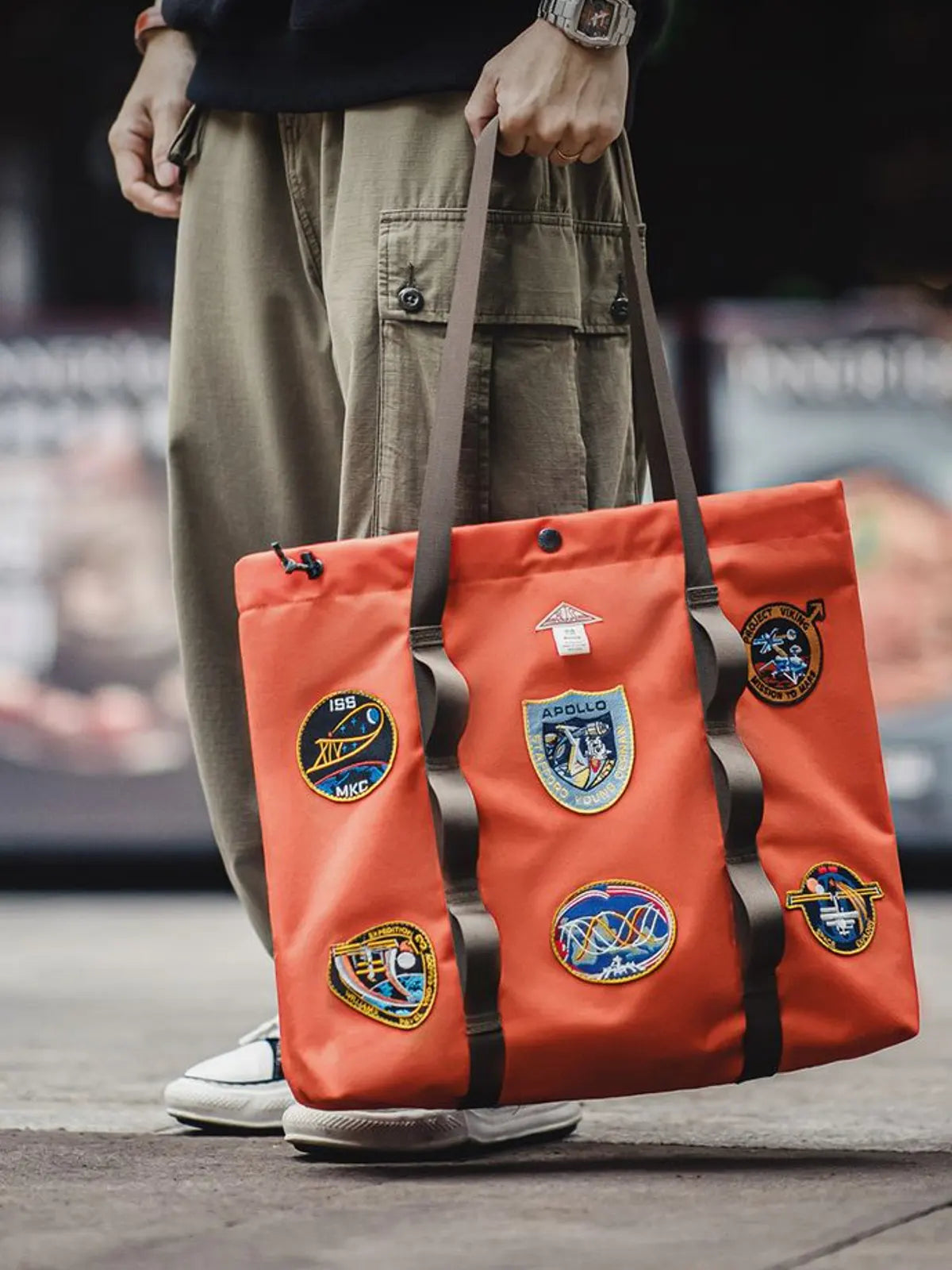アポロ号テーマの刺繍が施されたオレンジ色のナイロン製トートバッグ。大容量で機能性があり、デザイン性も高い。

