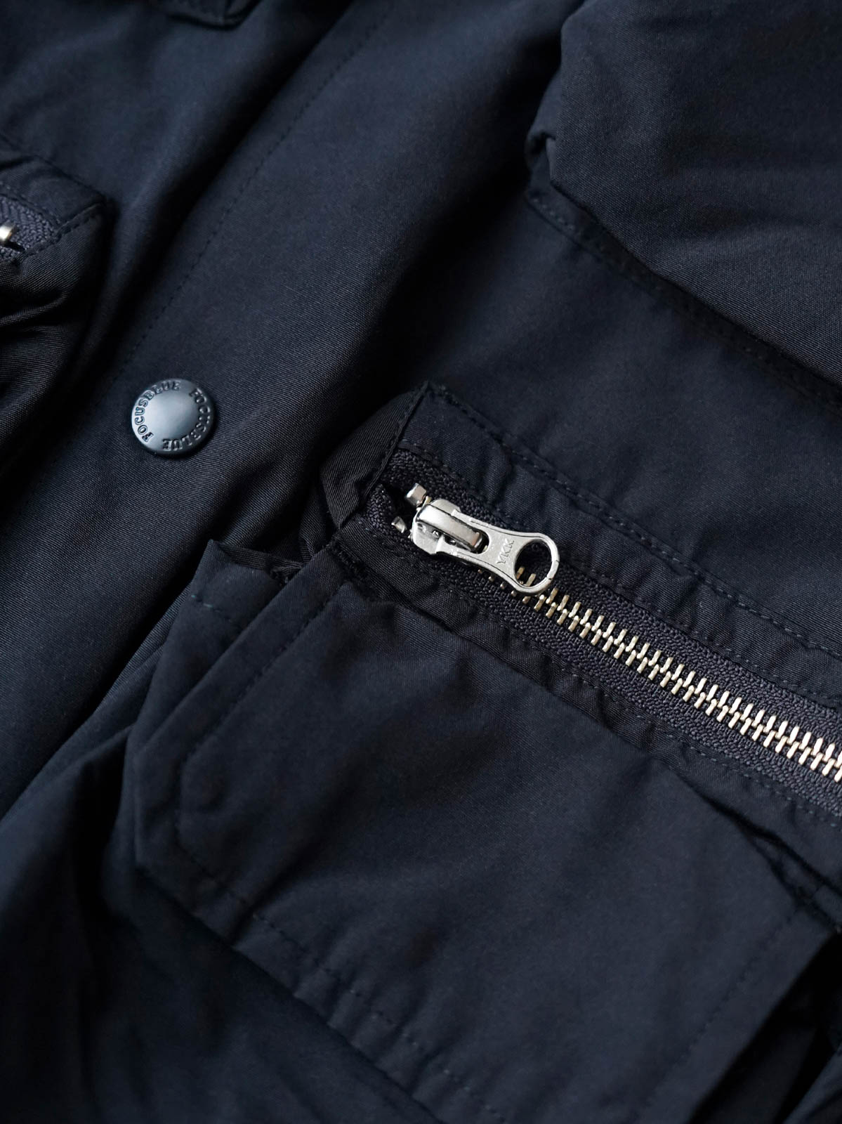 製品画像
「アシンメトリーデザインの多ポケットキャンプワークジャケット全体の展示図。クラシックなフィッシングジャケットとワークスタイルが融合したデザインで、ユニークなアシンメトリーデザインが実用性と個性を強調。防撥水機能を備えたポリエステルとコットン混紡生地を使用し、快適な着心地を提供します。」

詳細画像
「胸元のロゴ刺繍とアシンメトリーな多機能ポケットのディテール特写。YKKカスタムジッパーとロゴ入りスナップボタンが、高品質のディテールを引き立て、機能性とスタイルを両立させています。ダブルレイヤーのリブ編みが施され、袖口と裾のフィット感と耐久性を向上させています。」
