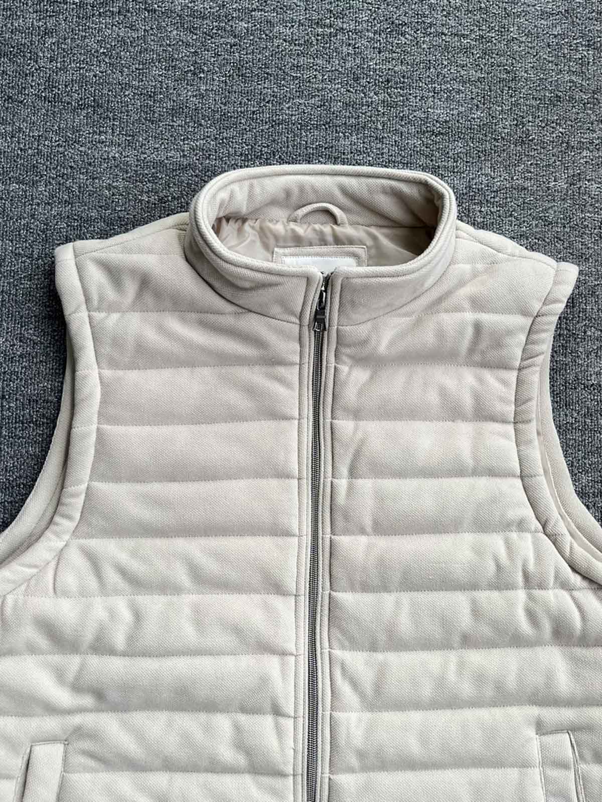 製品画像: 中綿入りの無地スタンドカラーのベスト正面ビュー。シンプルでスタイリッシュなデザインと、中綿素材の保温効果が際立つ。
詳細画像: 中綿入りベストのスタンドカラーと中綿素材のディテール。冬の寒さから守るための中綿素材とスタンドカラーの特徴が明確に見える。