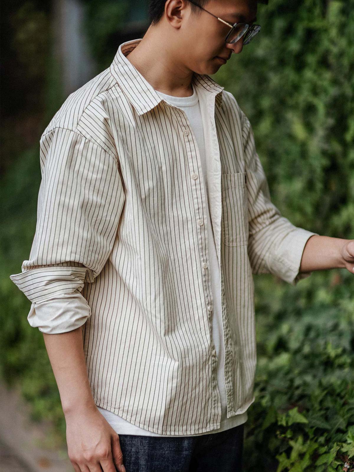 詳細画像: 細ストライプとダブルボタンカフスのディテール
モデル画像: 細ストライプのゆったりシルエットシャツを着用した男性