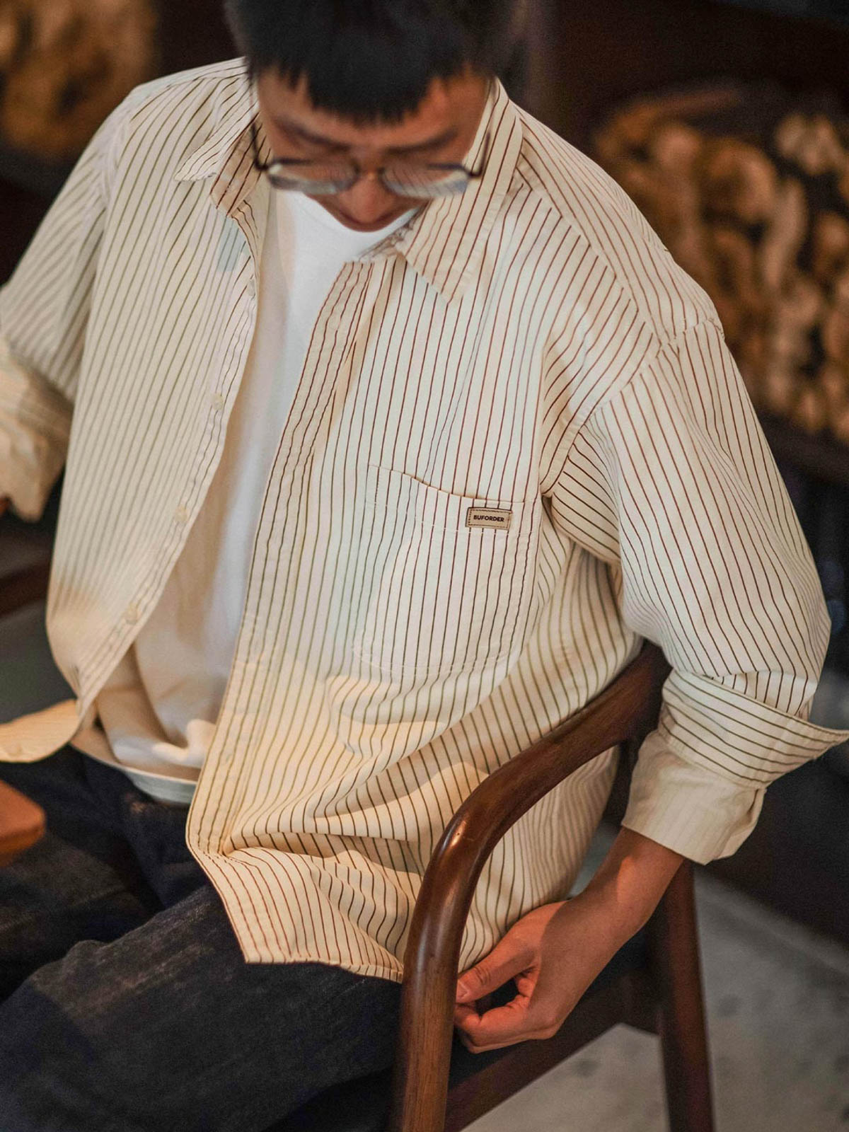 詳細画像: 細ストライプとダブルボタンカフスのディテール
モデル画像: 細ストライプのゆったりシルエットシャツを着用した男性