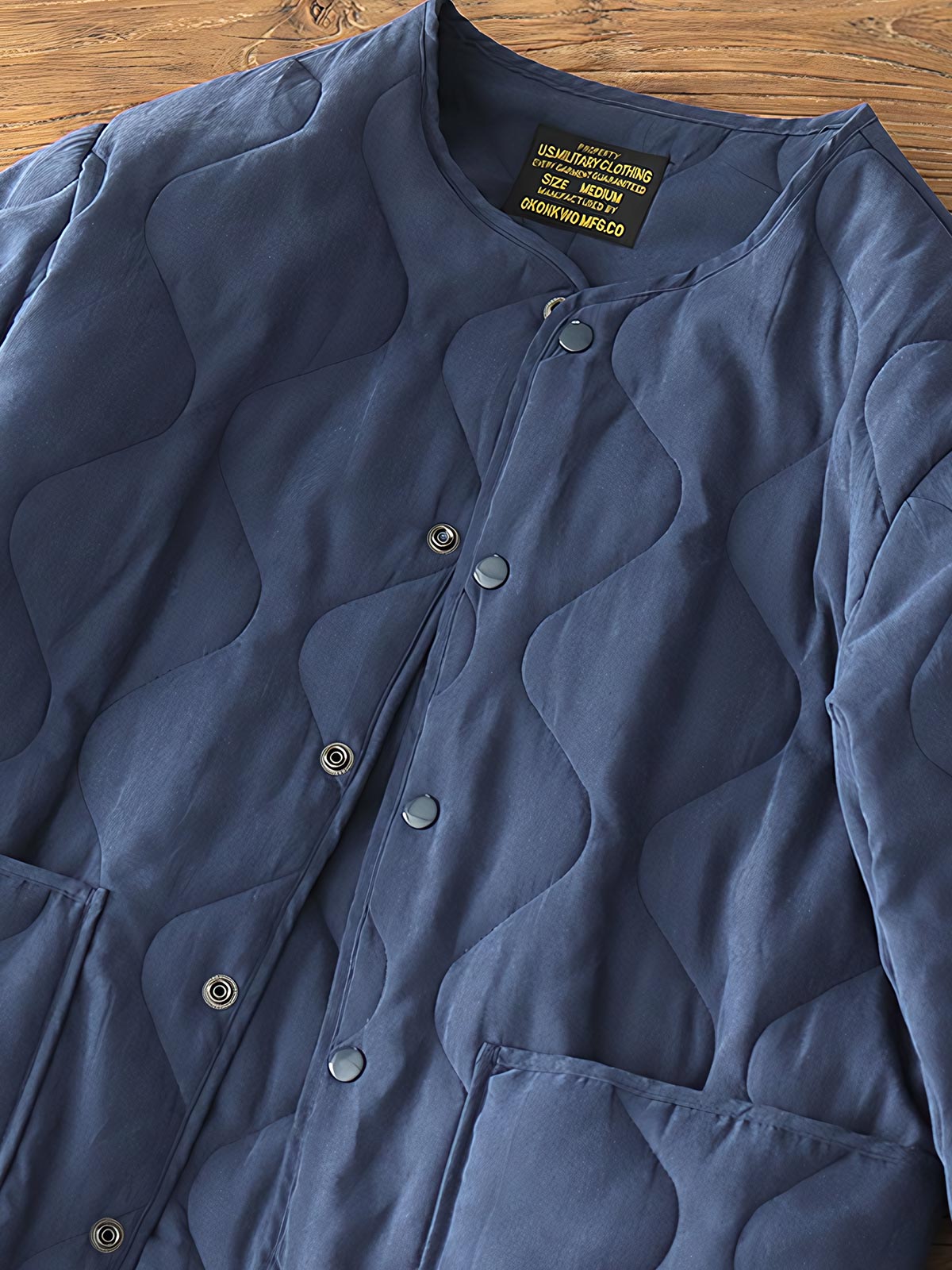 製品画像: M65ライナーリニューアルコートの全体展示。柔らかな両面ピーチスキンとウォッシュドコットン中綿を使用し、秋冬のアウターに最適な暖かさと快適さを提供するノーカラーデザイン。
詳細画像: 独特なウェーブキルティングディテールが施されたM65ライナーコート、シワになりにくいピーチスキン素材の質感。