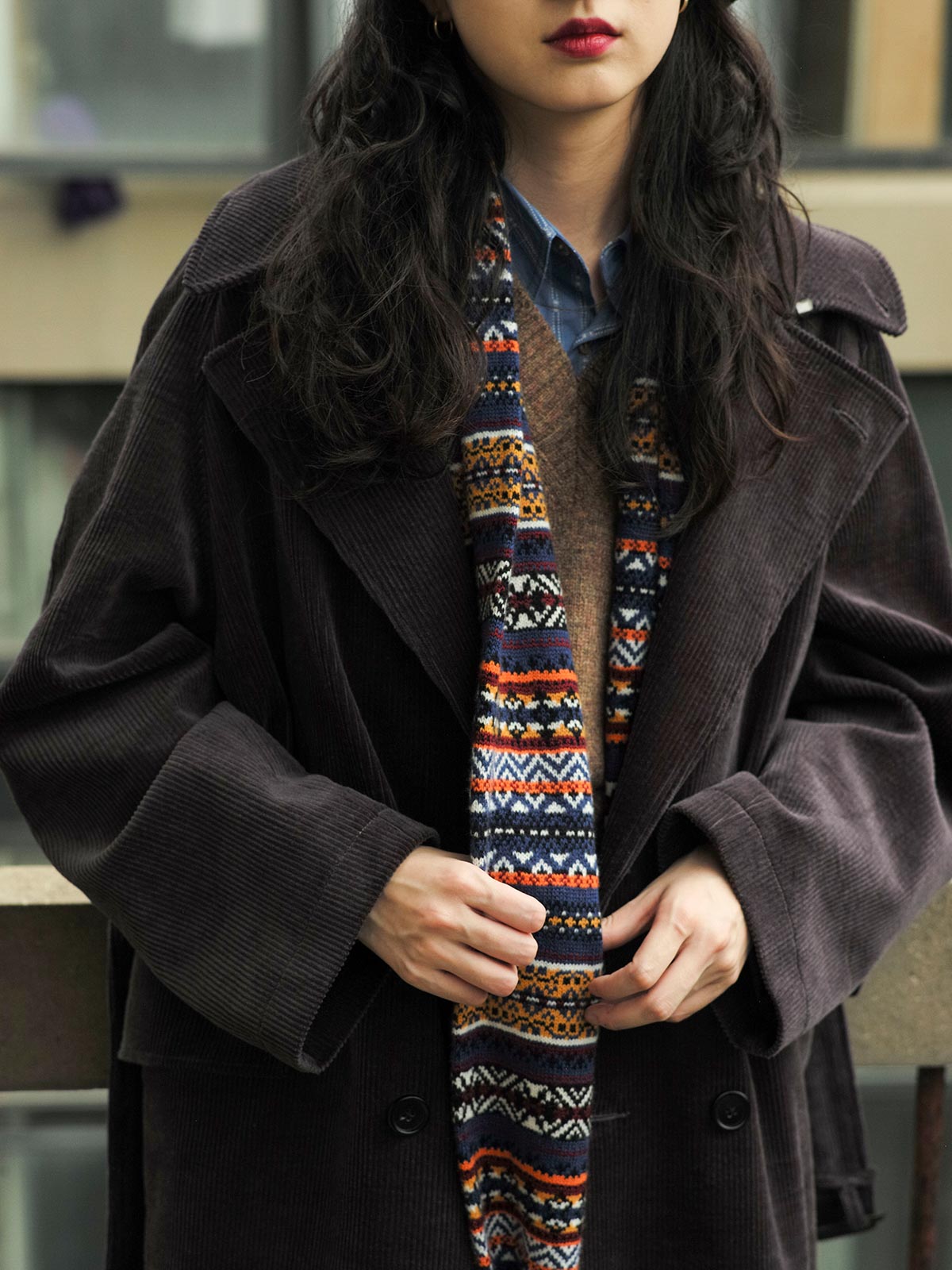 詳細画像：マフラーの織り目とフェアアイランド柄のディテールが鮮明に描かれており、シェトランドウール特有の柔らかな質感と耐久性が伝わります。染色技術にこだわったカラフルな糸が、アクセントとなる美しいデザインを際立たせています。

モデル画像：シェトランドウールのフェアアイランド柄マフラーを着用したモデルが、ヴィンテージ感のあるスタイルでコーディネートしています。マフラーの柔らかさと温かさが際立ち、日常的なカジュアルスタイルにもぴったりのアイテムであることを示しています。