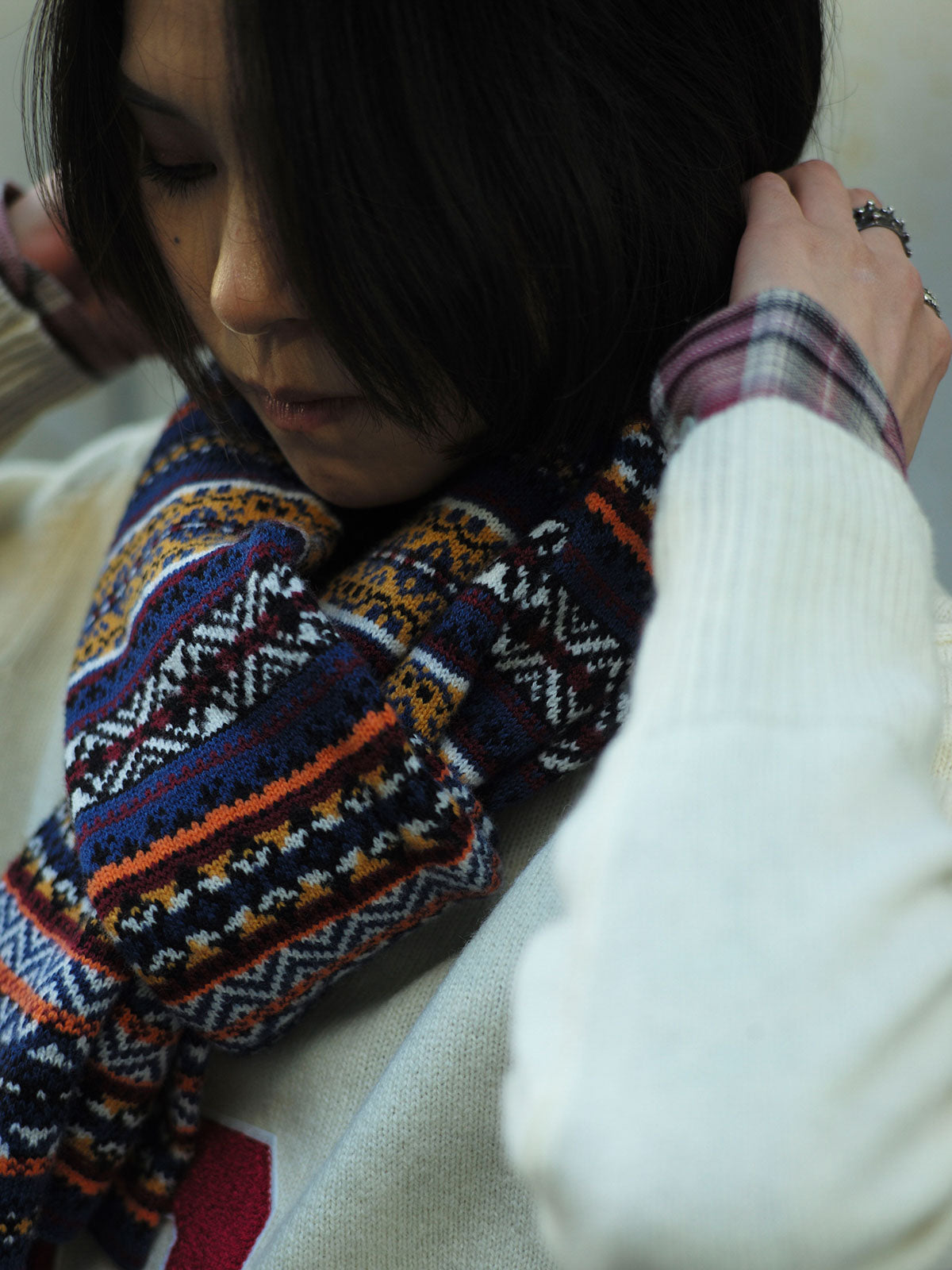 詳細画像：マフラーの織り目とフェアアイランド柄のディテールが鮮明に描かれており、シェトランドウール特有の柔らかな質感と耐久性が伝わります。染色技術にこだわったカラフルな糸が、アクセントとなる美しいデザインを際立たせています。

モデル画像：シェトランドウールのフェアアイランド柄マフラーを着用したモデルが、ヴィンテージ感のあるスタイルでコーディネートしています。マフラーの柔らかさと温かさが際立ち、日常的なカジュアルスタイルにもぴったりのアイテムであることを示しています。