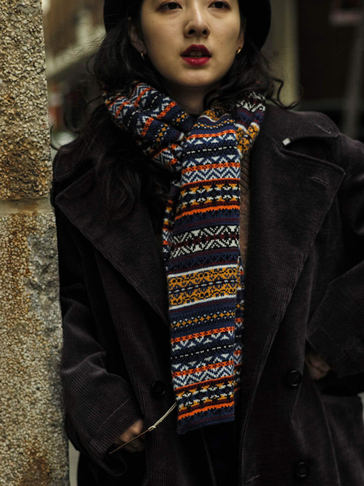 詳細画像：マフラーの織り目とフェアアイランド柄のディテールが鮮明に描かれており、シェトランドウール特有の柔らかな質感と耐久性が伝わります。染色技術にこだわったカラフルな糸が、アクセントとなる美しいデザインを際立たせています。

モデル画像：シェトランドウールのフェアアイランド柄マフラーを着用したモデルが、ヴィンテージ感のあるスタイルでコーディネートしています。マフラーの柔らかさと温かさが際立ち、日常的なカジュアルスタイルにもぴったりのアイテムであることを示しています。