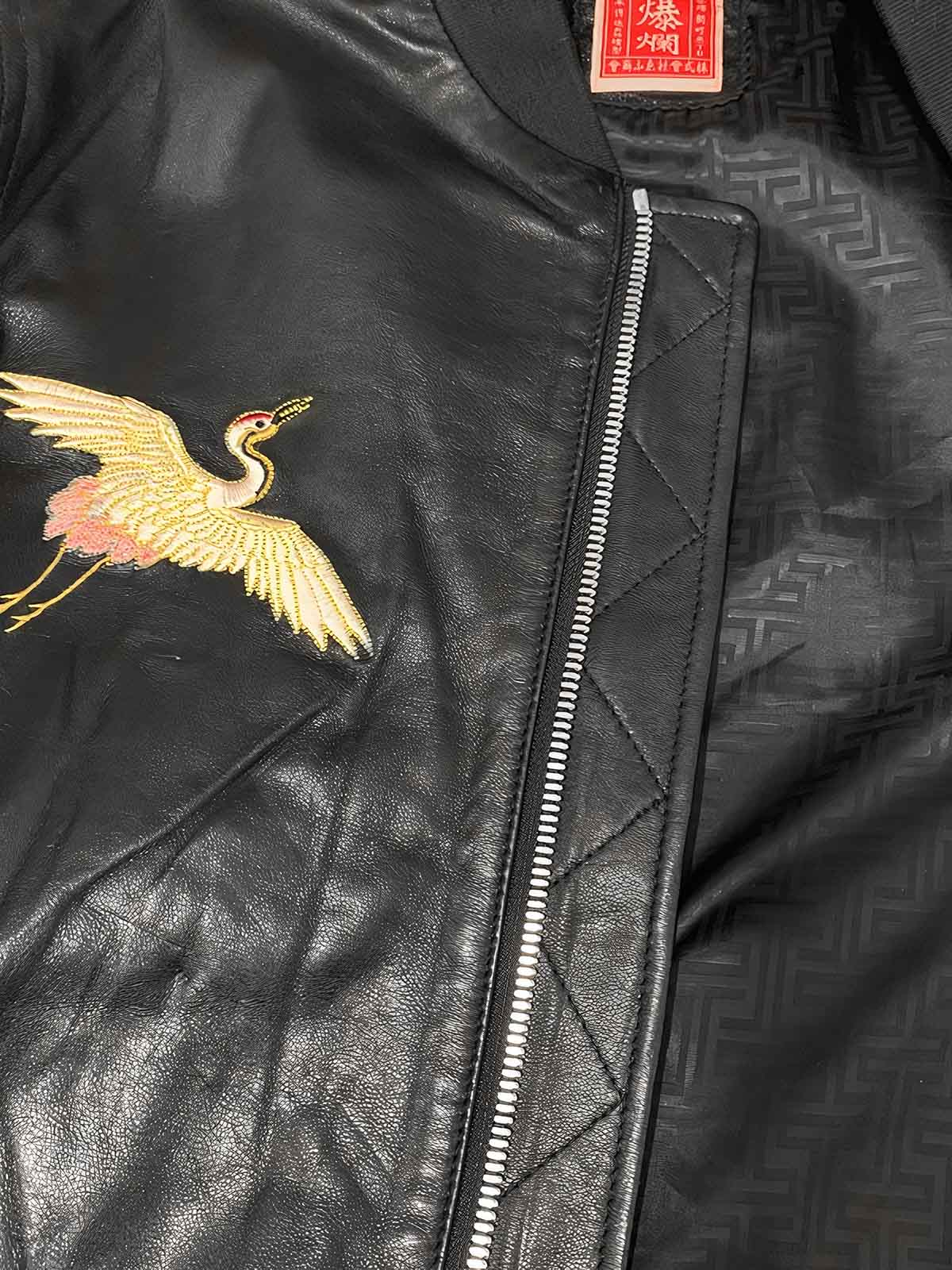 製品画像: 横須賀鶴図刺繍 羊革ジャケット全体画像、吉祥の象徴である「鶴図」刺繍と上質な輸入羊革のデザイン
詳細画像: 横須賀の伝統技法を用いた鶴、松、雲の刺繍ディテール、立体感ある精巧な工芸