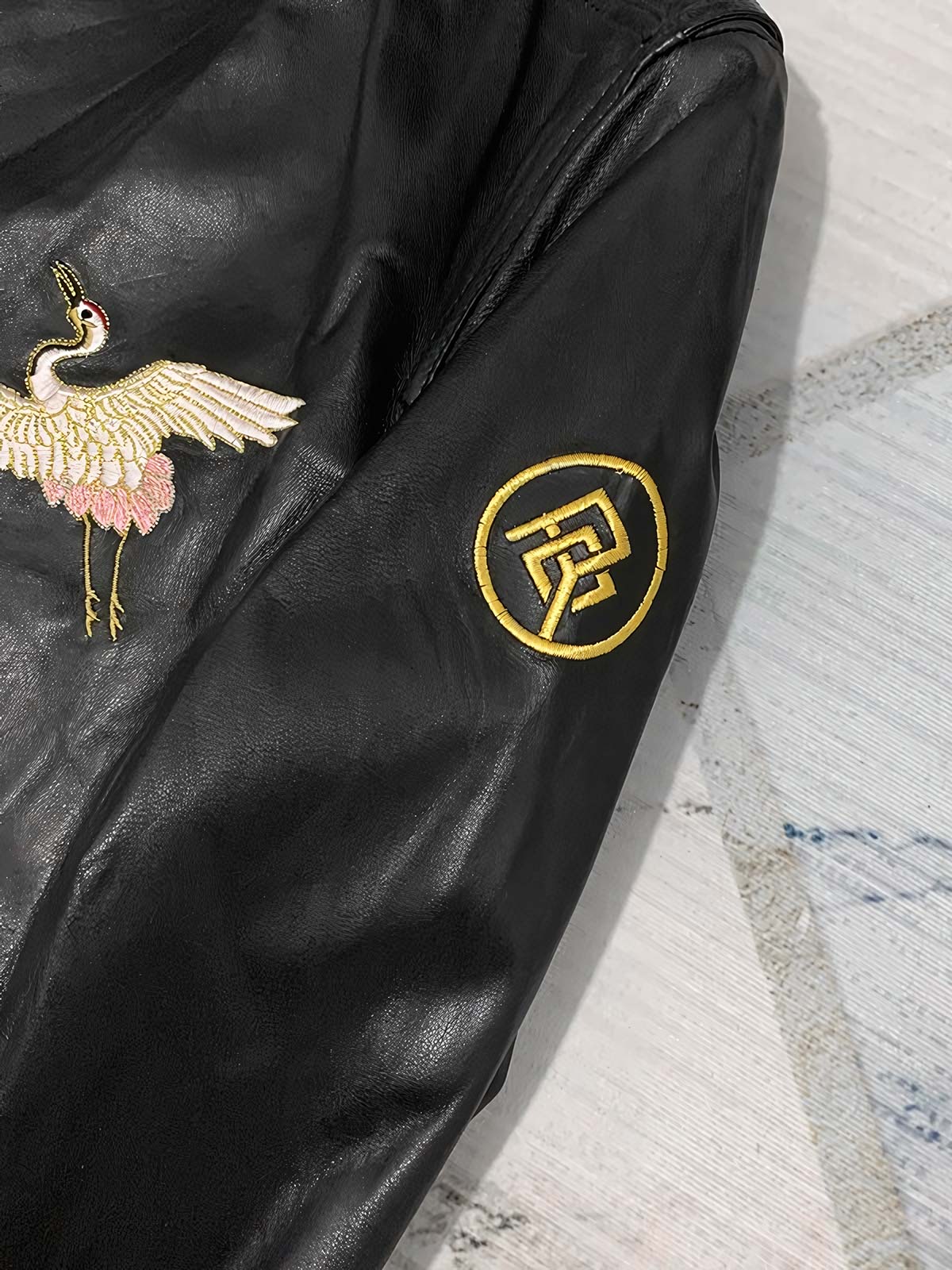 製品画像: 横須賀鶴図刺繍 羊革ジャケット全体画像、吉祥の象徴である「鶴図」刺繍と上質な輸入羊革のデザイン
詳細画像: 横須賀の伝統技法を用いた鶴、松、雲の刺繍ディテール、立体感ある精巧な工芸