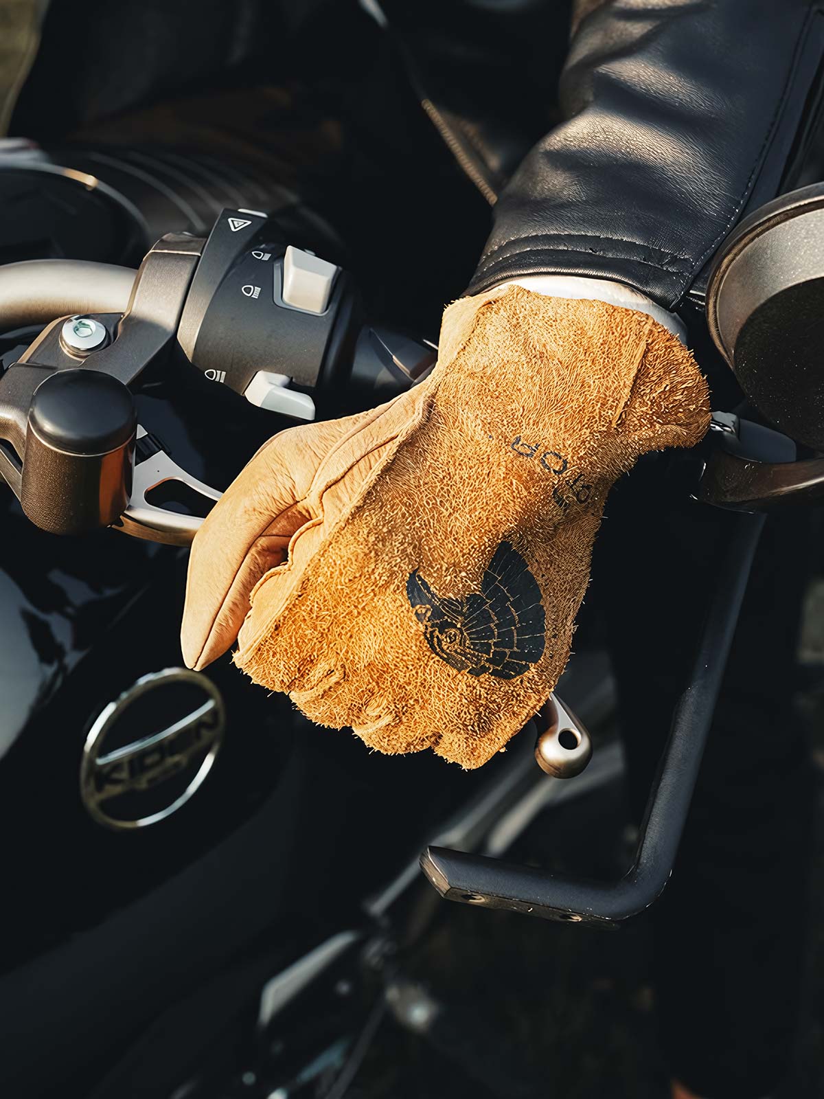 詳細画像
グローブのディテールと素材感アップ。マットレザーを使用した手袋の細部が強調されており、特にダブルステッチや鷲の目のデザインが、製品の耐久性と独特な個性を引き立てています。手に馴染む柔らかな質感や、ヴィンテージの風合いが美しく表現されています。
モデル画像
モデルがマットレザーのバイカーズグローブを着用したライディングスタイル。バイカーズグローブのデザインやフィット感が実際の使用シーンでどのように活かされるかがわかります。ライダーにとって必要な機能性とファッション性を兼ね備えたアイテムで、アウトドアや日常のライディングに最適です。