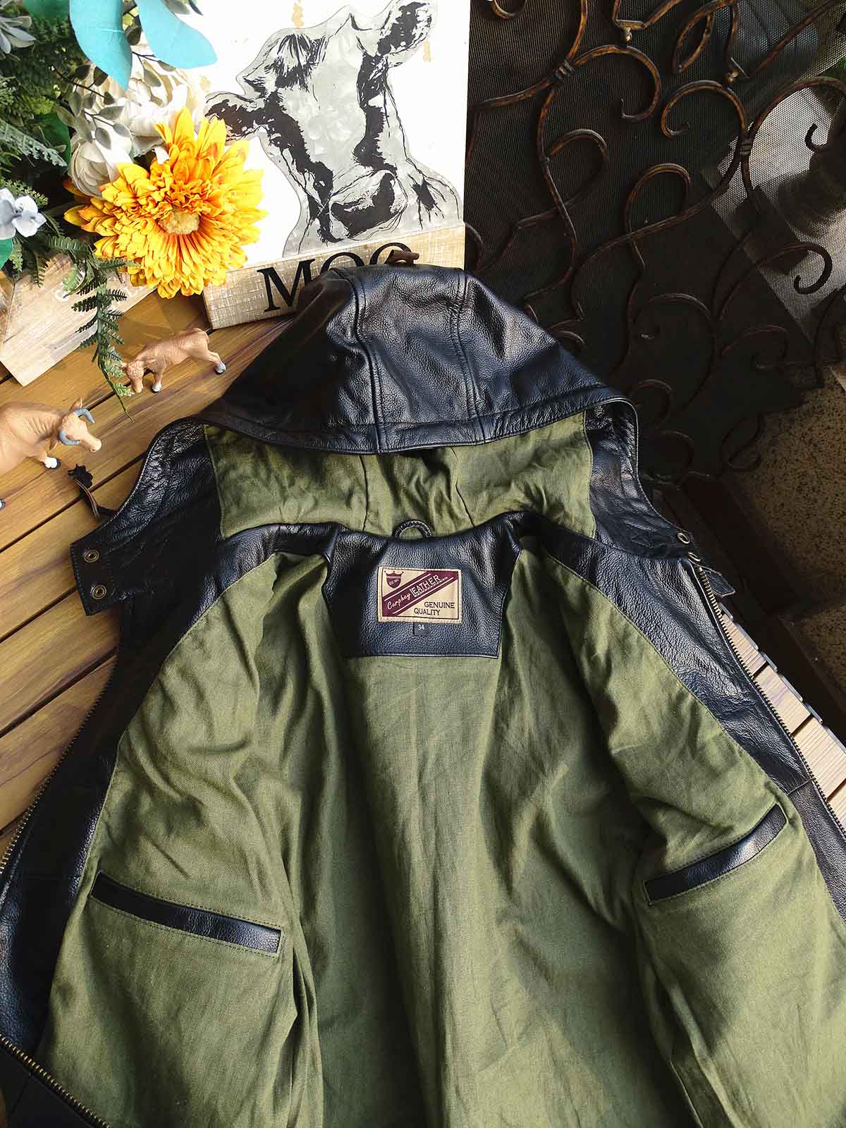 製品画像： 9ポケットフィールドフード付きフルグレインレザージャケット全体イメージ画像。黒いシボ加工レザーとヴィンテージ感漂うオイル仕上げのスエードディテールが特徴で、アウトドアやバイクライドにも適した多機能デザイン。
詳細画像： YKKアンティークブロンズジッパーとオイルドスエードレザーの補強ディテールをクローズアップした画像。耐久性とクラシックな風合いが際立つ仕上がり。