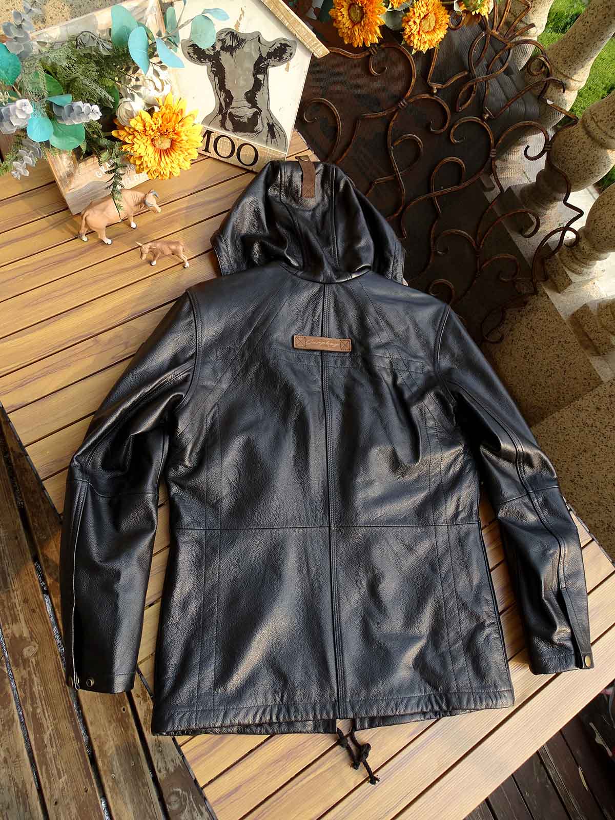 製品画像： 9ポケットフィールドフード付きフルグレインレザージャケット全体イメージ画像。黒いシボ加工レザーとヴィンテージ感漂うオイル仕上げのスエードディテールが特徴で、アウトドアやバイクライドにも適した多機能デザイン。
詳細画像： YKKアンティークブロンズジッパーとオイルドスエードレザーの補強ディテールをクローズアップした画像。耐久性とクラシックな風合いが際立つ仕上がり。