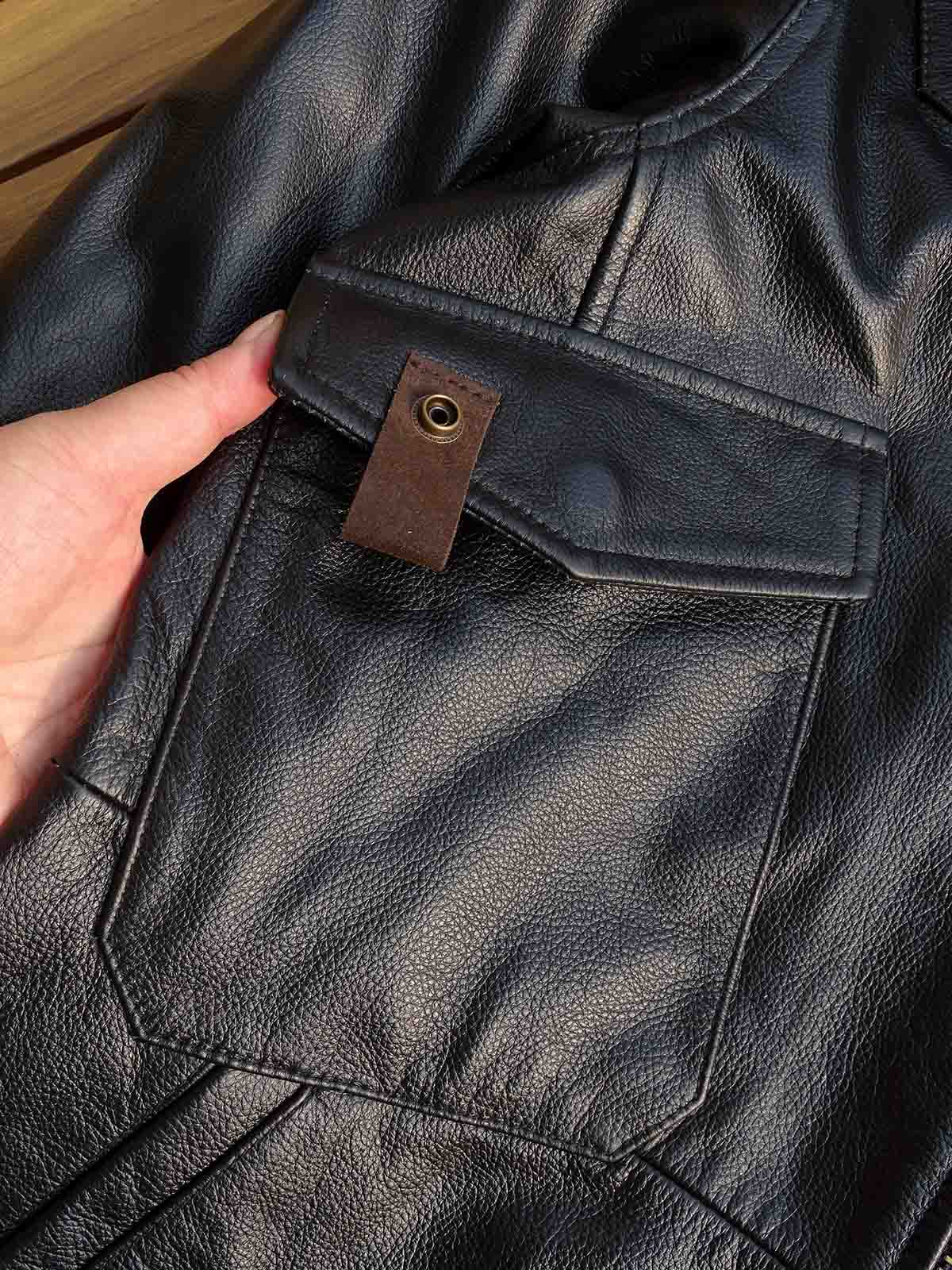 製品画像： 9ポケットフィールドフード付きフルグレインレザージャケット全体イメージ画像。黒いシボ加工レザーとヴィンテージ感漂うオイル仕上げのスエードディテールが特徴で、アウトドアやバイクライドにも適した多機能デザイン。
詳細画像： YKKアンティークブロンズジッパーとオイルドスエードレザーの補強ディテールをクローズアップした画像。耐久性とクラシックな風合いが際立つ仕上がり。