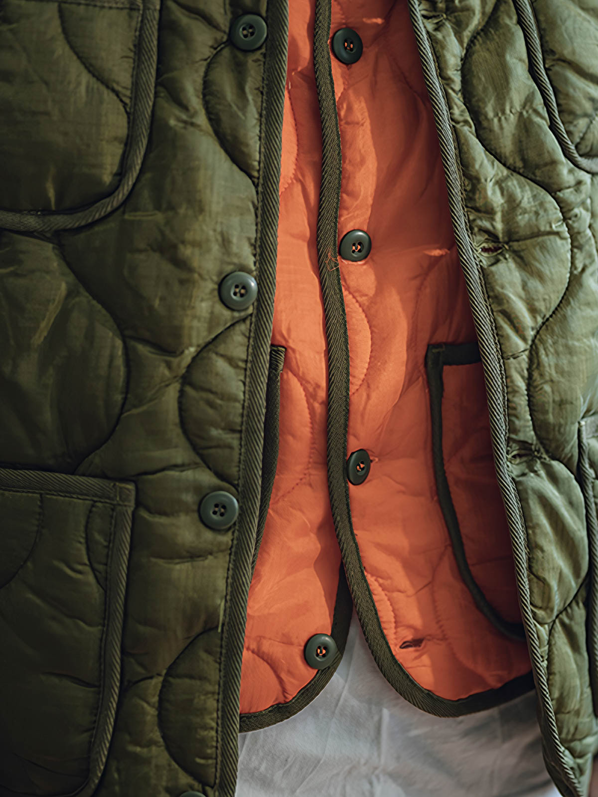 詳細画像: リバーシブルデザイン（オリーブグリーンとレスキューオレンジ）、袖口のリブ編みが冷気をシャットアウト。軽量でありながら優れた保温性を提供。

モデル画像: モデルが弧形キルティングインナーダウンジャケットを着用、ルーズフィットシルエットと防水性に優れた素材で、秋冬のレイヤードスタイルを演出。