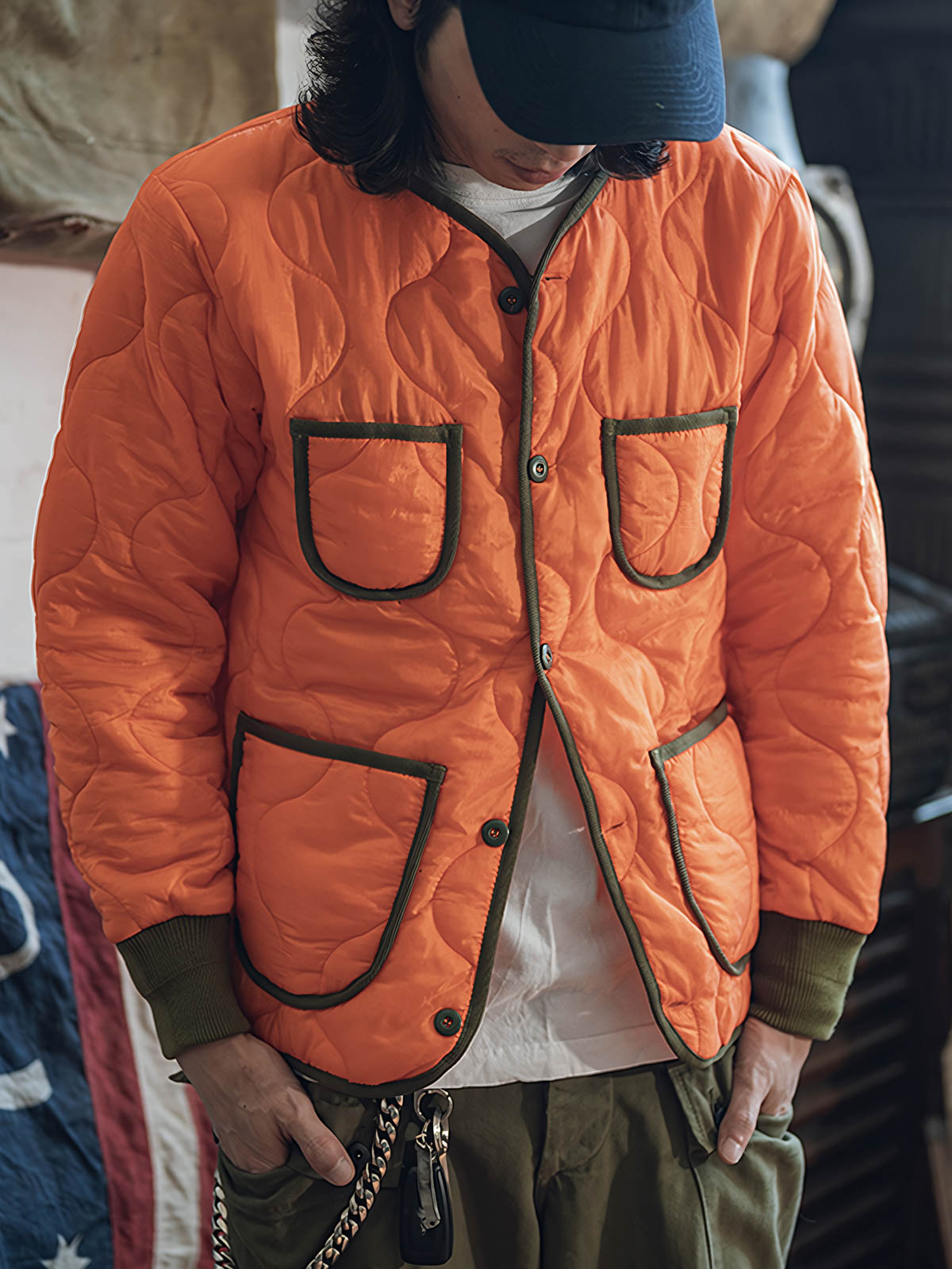 詳細画像: リバーシブルデザイン（オリーブグリーンとレスキューオレンジ）、袖口のリブ編みが冷気をシャットアウト。軽量でありながら優れた保温性を提供。

モデル画像: モデルが弧形キルティングインナーダウンジャケットを着用、ルーズフィットシルエットと防水性に優れた素材で、秋冬のレイヤードスタイルを演出。