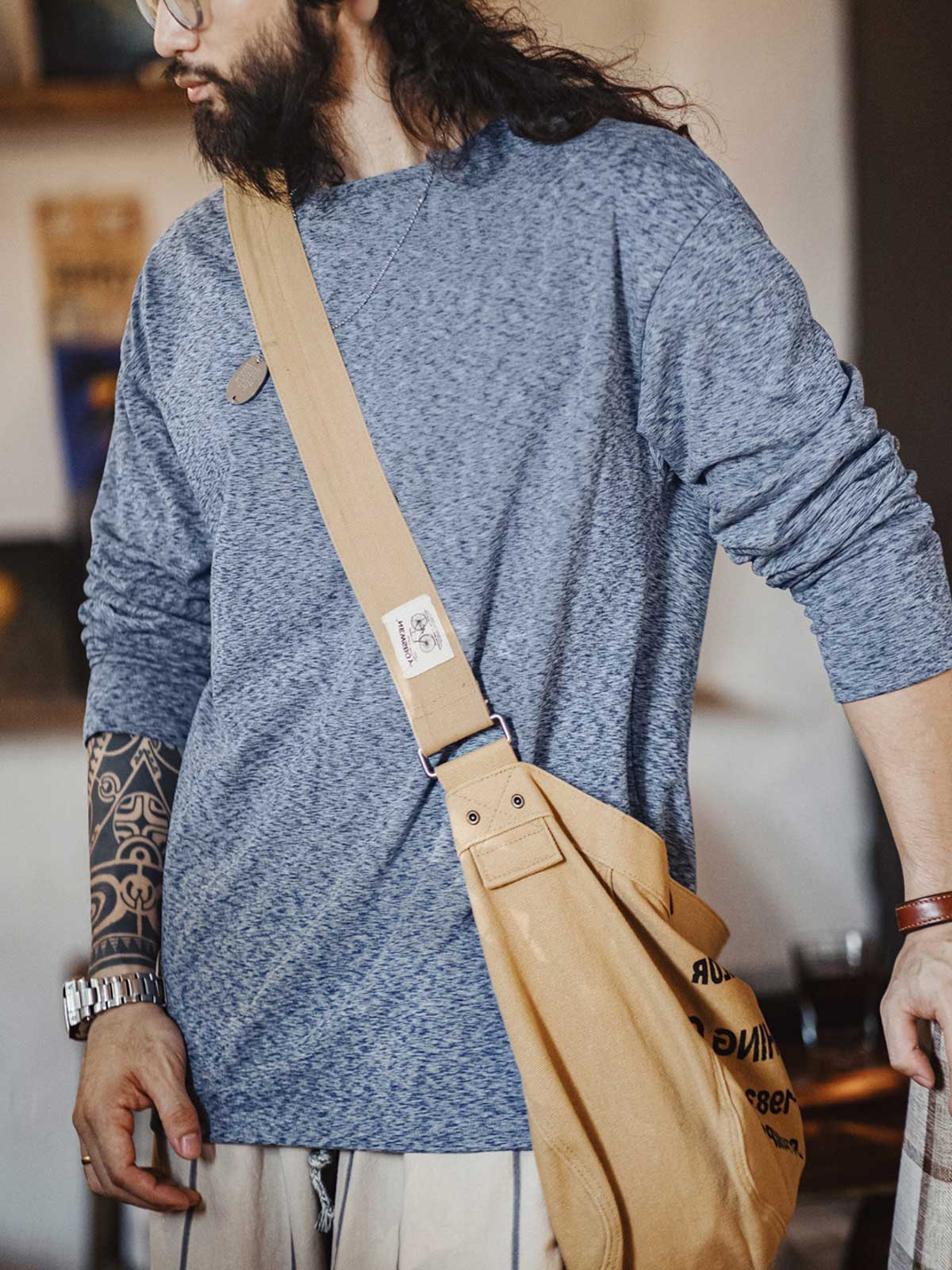 詳細画像: カチオン糸による独特な風合いとヴィンテージ感漂うブラウンのレザーパッチのディテールをクローズアップした画像。見た目の個性と高級感を強調。
モデル画像: 両面フリース起毛 長袖Tシャツを着用したモデルが、リラックスしたカジュアルコーディネートを披露。インナーとしても単独でも活躍するアイテム。
