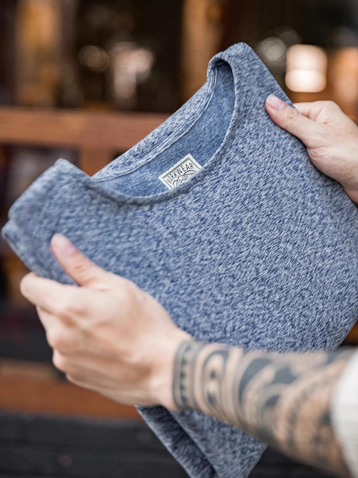 製品画像: 両面フリース起毛 クルーネック 長袖Tシャツの全体展示画像。柔らかく暖かい両面起毛素材とカチオン二色糸のデザインが特徴で、秋冬シーズンに最適なアイテム。
詳細画像: カチオン糸による独特な風合いとヴィンテージ感漂うブラウンのレザーパッチのディテールをクローズアップした画像。見た目の個性と高級感を強調。