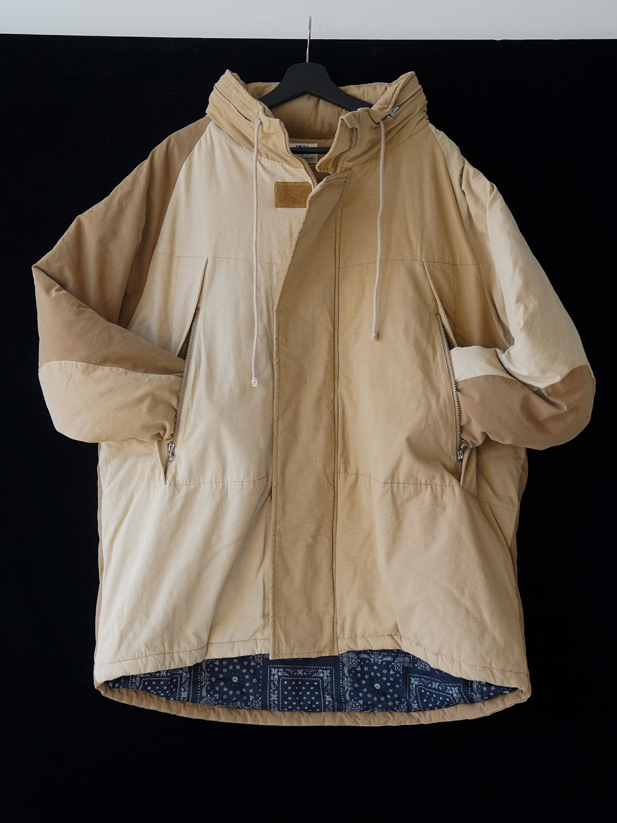 詳細画像
「ペイズリー柄の裏地と日本製YKK製の両開きファスナーのディテールを特写した画像。ヴィンテージデザインと高機能性を兼ね備えたジャケット。」

モデル画像
「モデルがトーンオントーン パッチワーク ミドル丈中綿ジャケットを着用し、デニムパンツと合わせた冬のアウトドアカジュアルスタイルを披露。」