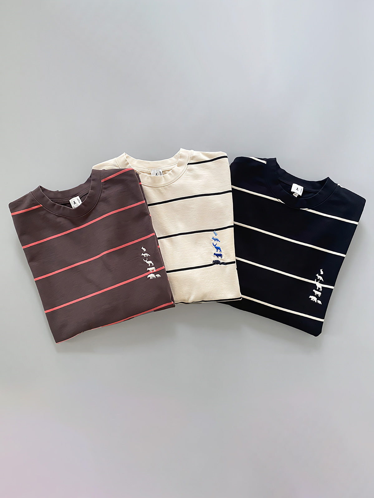 製品画像
ヴィンテージ感あふれるストライプパターンが特徴のヘビーウェイト長袖Tシャツ。胸元に高密度刺繍で描かれた動物たちが自然の童話を語るようなデザインで、青春の記憶とクラシックなエレガンスを融合した一枚

詳細画像
森の動物たちをモチーフにした高密度刺繍のディテールと、320gのヘビーウェイトコットンが織りなすヴィンテージ感ある質感が魅力。刺繍の精巧さと厚手の生地が時代を超えた価値を表現