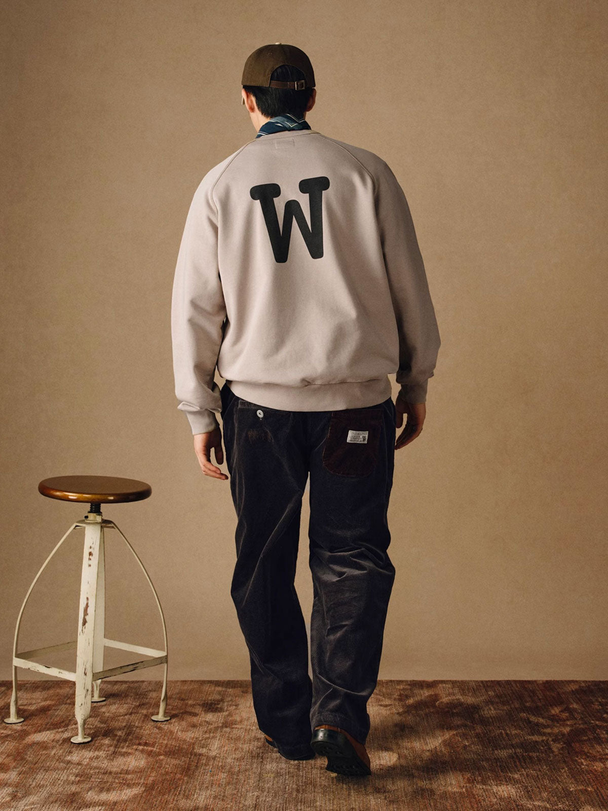 詳細画像
「胸元の英文字プリントとスノーウォッシュ加工による色落ち感が際立つ生地のディテールクローズアップ。柔らかな肌触りと褪色の質感が魅力。」

モデル画像
「モデルがピンクベージュの色落ち加工スウェットを着用し、カジュアルパンツと合わせたレトロでスポーティなヴィンテージ風コーディネート。」