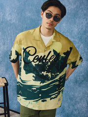 モデルが雪山流水デザインのハワイアンシャツを着用し、カジュアルショーツと組み合わせたスタイリングを示す画像。