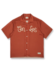 オレンジレッドの背景にレトロプリントが施されたキューバカラーの半袖シャツの正面ビュー。直線的でゆったりとしたカットが特徴で、リラックスしたカジュアルスタイルを提供します。