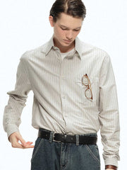 詳細画像: ブルーの細ストライプと胸元のポケットディテール特写、ヴィンテージカットが強調された部分
モデル画像: モデルが100%コットンストライプシャツを着用し、シンプルでヴィンテージ感のあるカジュアルスタイルを披露