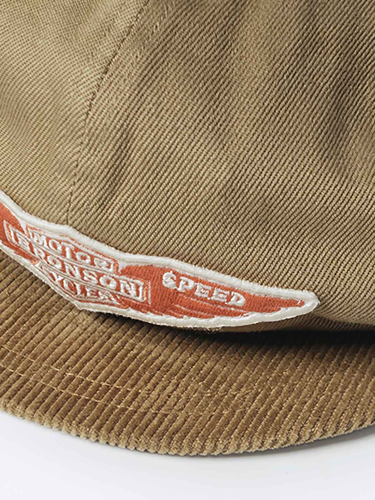 キャップのエラスティックバンド固定デザインと低彩度オレンジ色のバッジのクローズアップ。