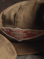 キャップのエラスティックバンド固定デザインと低彩度オレンジ色のバッジのクローズアップ。