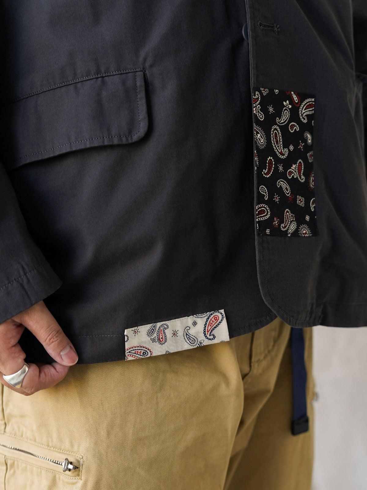 詳細画像
「不規則に配置されたペイズリー柄パッチと高密度ヘリンボーン裏地のディテールクローズアップ。機能性とファッション性を融合したデザイン。」

モデル画像
「モデルがヴィンテージ ペイズリー柄パッチルーズフィット テーラードジャケットをデニムパンツとスニーカーに合わせたリラックスしたカジュアルコーディネート。」