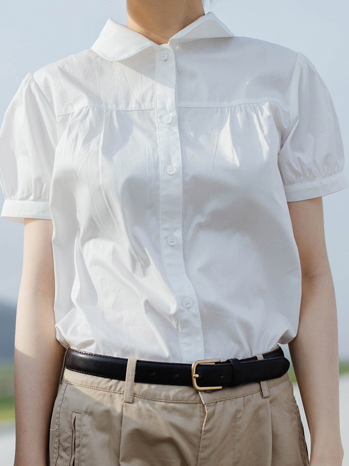 モデルが白色ピーターパンカラーシャツを着用し、シックなスタイルを披露