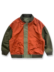 製品画像: リバーシブルジャケット（アーミーグリーン面）の全体展示図。表面にはアーミーグリーンのシンプルで落ち着いたデザイン、裏面には鮮やかなオレンジ色のアクセントが施されており、両面で異なるスタイルが楽しめる。
詳細画像: リバーシブルジャケットの表裏切り替えデザインとジッパー装飾ディテールの特写。防風防水機能素材で春秋の天候に対応し、実用性とスタイルを両立。