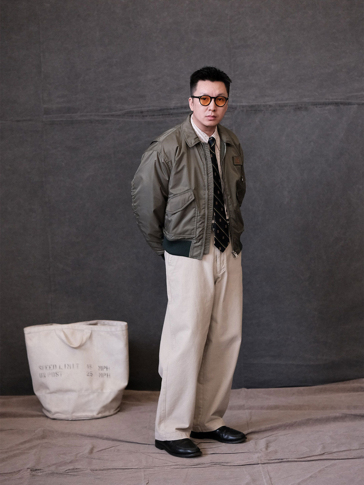 詳細画像:
TALONメタルジッパーとマジックテープエンブレムのディテール。レトロ感あふれるエンブレムとジッパーが、クラシックなフライトジャケットの魅力を引き立てます。
モデル画像:
モデルがCWU-45Pフライトジャケットを着用し、ジーンズやカーゴパンツと合わせたクラシックなミリタリースタイルを披露している画像。